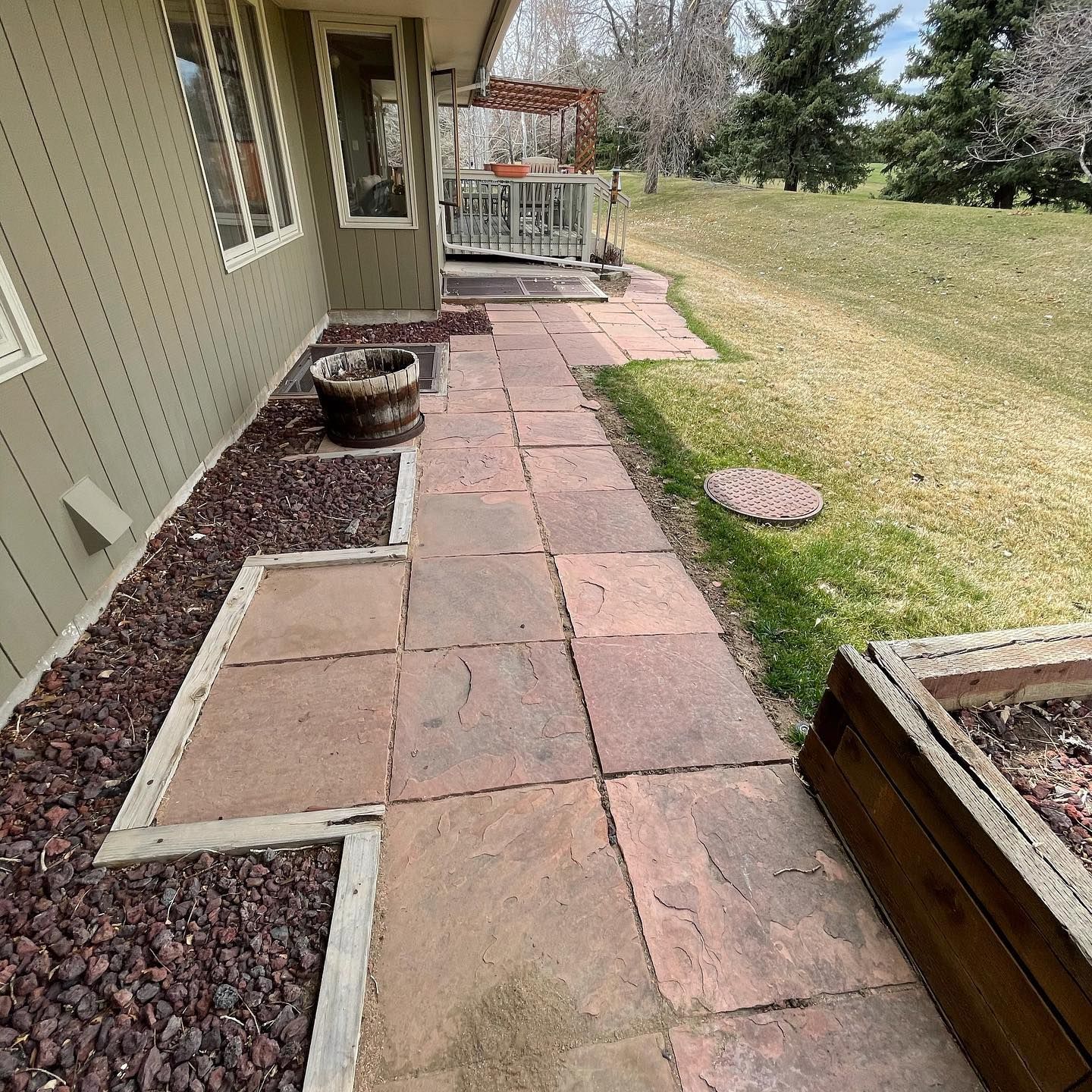 Stone patio walkway beside a house, with planters and a grassy yard in the background
