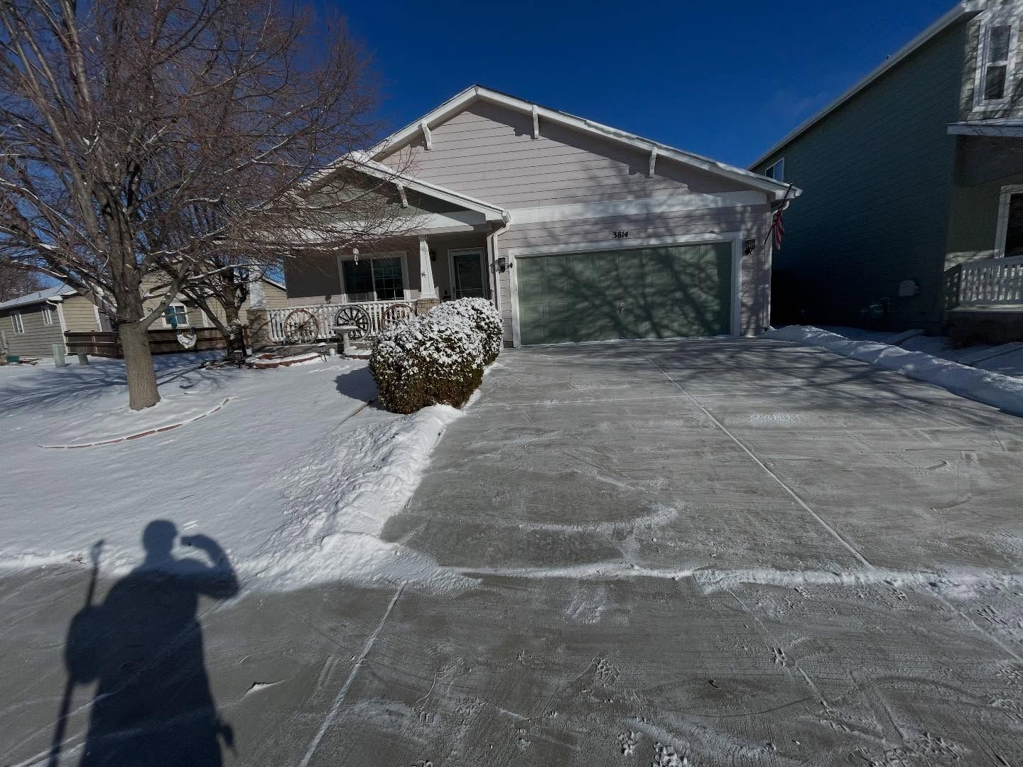 Snow-covered suburban driveway leading to a white house with a garage under a clear blue sky.