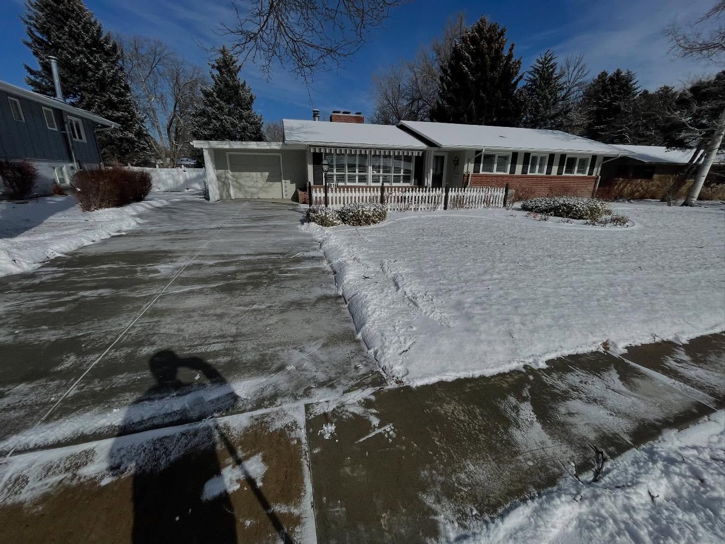 Snow-covered suburban house with a cleared driveway and walkway under a bright blue sky