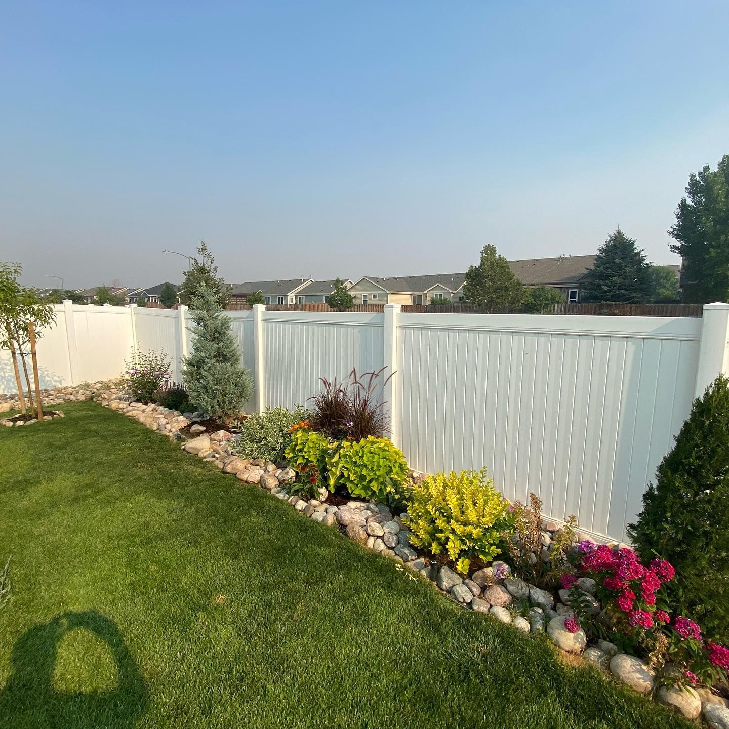 Backyard garden with white fence, green lawn, and colorful flowers along a stone border