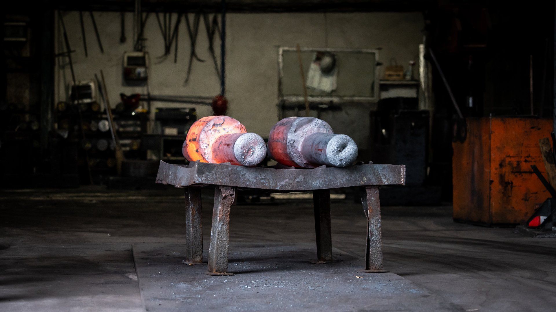 Tre forme colorate avvolte nel filato su una panca consumata in una penombra officina industriale.