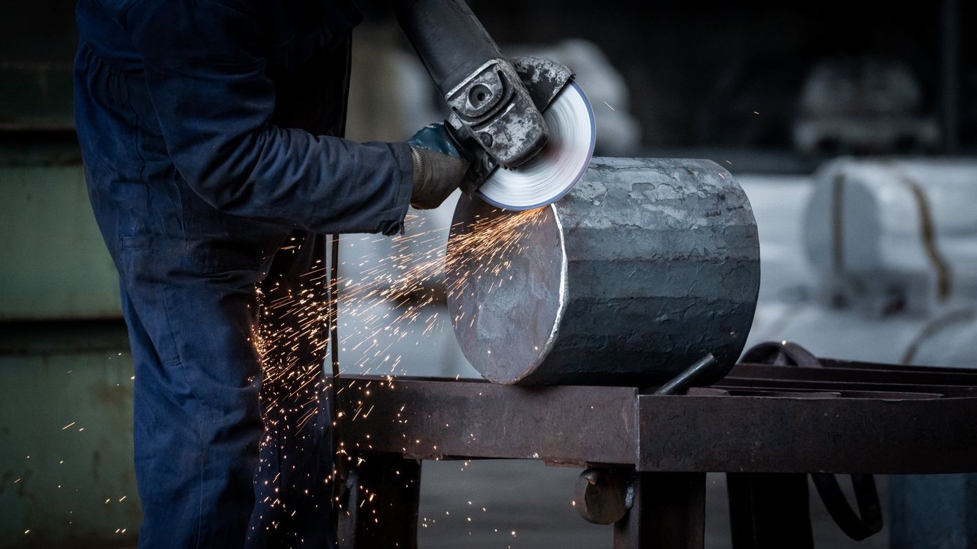 Un operaio utilizza una smerigliatrice angolare su un tubo metallico, generando scintille luminose in un'officina.