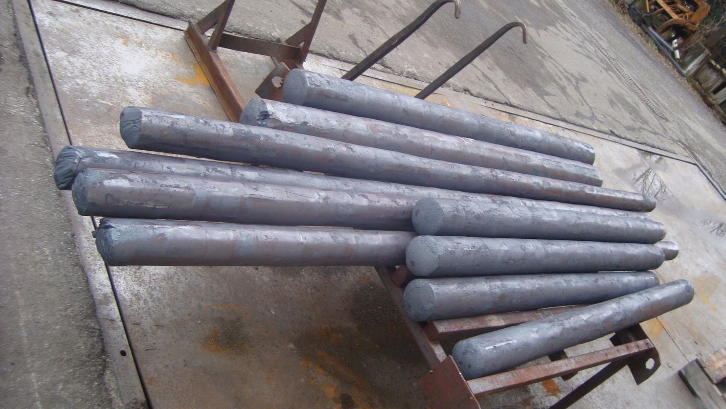Pila di tubi metallici grigi posati su una superficie di cemento all'aperto.