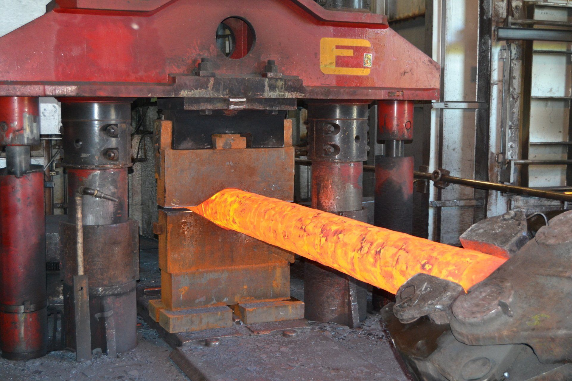 Una barra di metallo incandescente viene estratta da una pressa industriale per la forgiatura in una fabbrica.