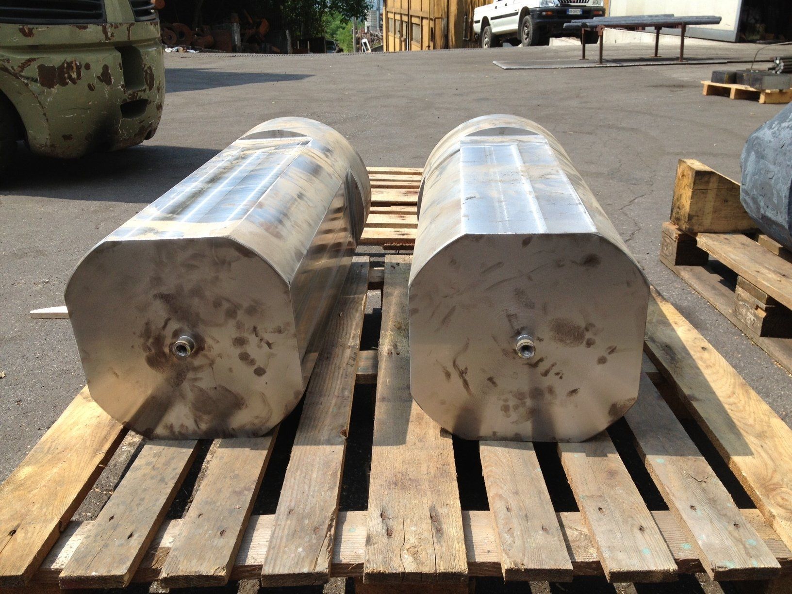 Due grandi serbatoi cilindrici in metallo argentato su un pallet di legno in un piazzale industriale all'aperto.