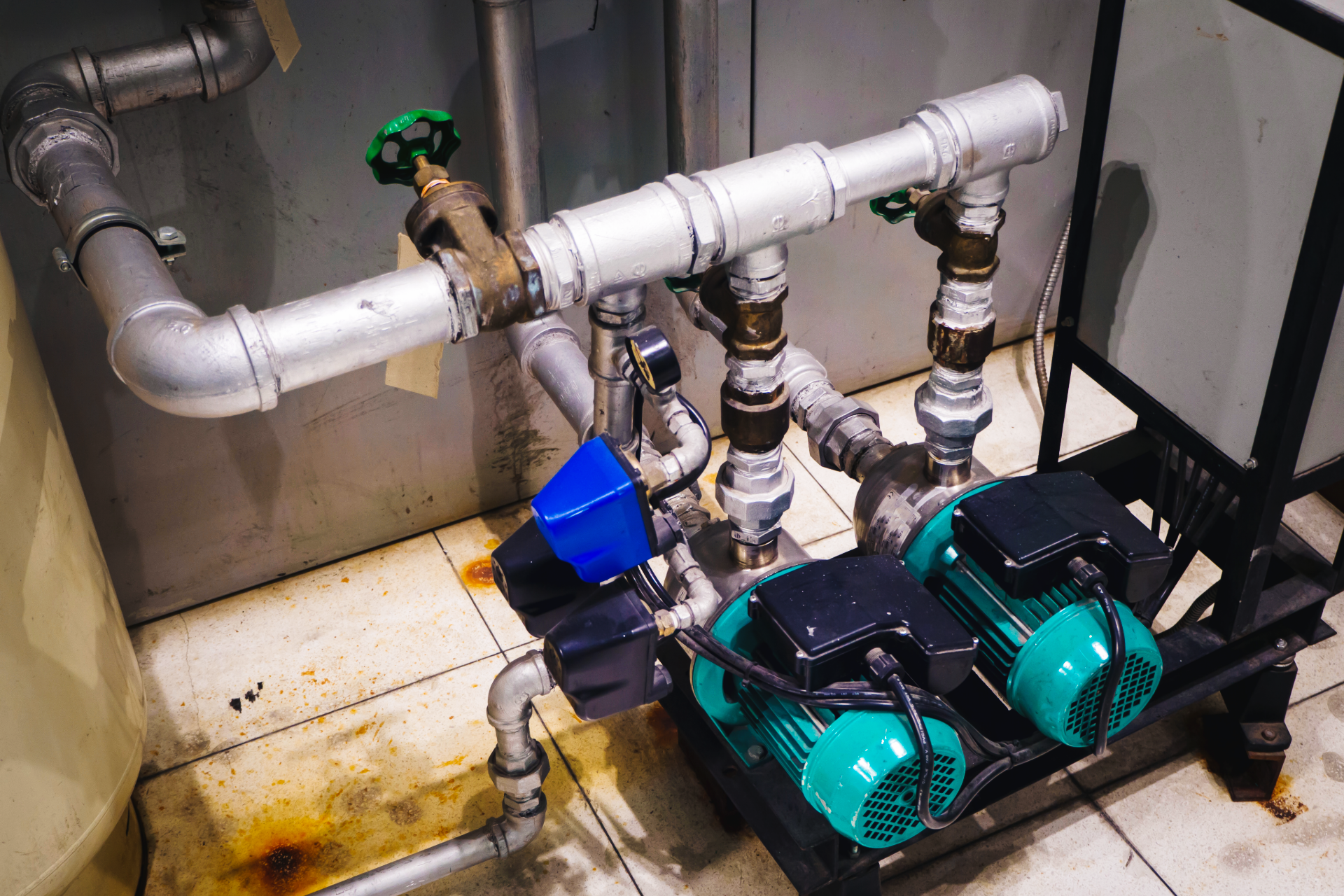Industrial pump and piping system with teal motors and white pipes in a utility room