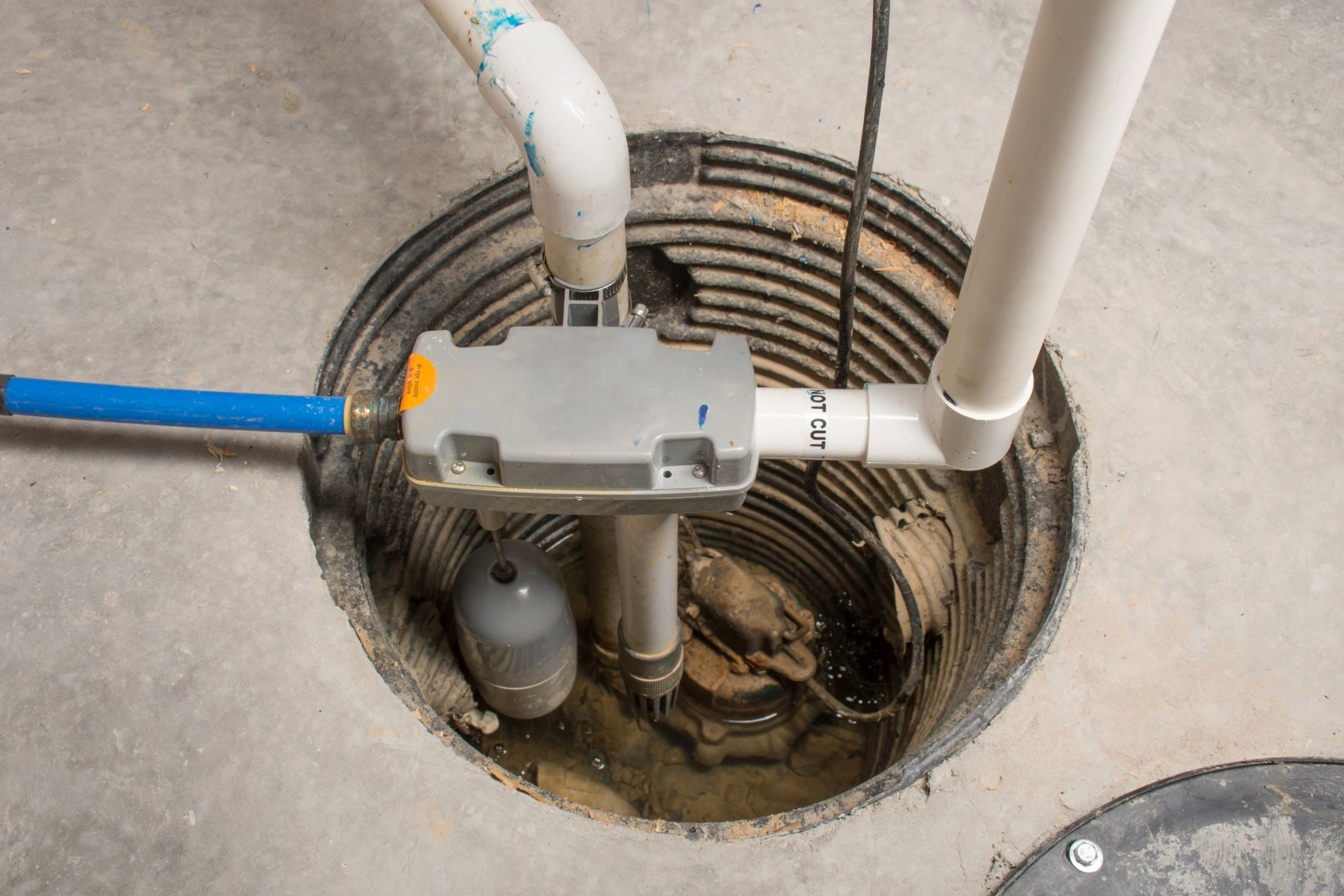 Sump pump with pipes and float switch in a concrete pit.