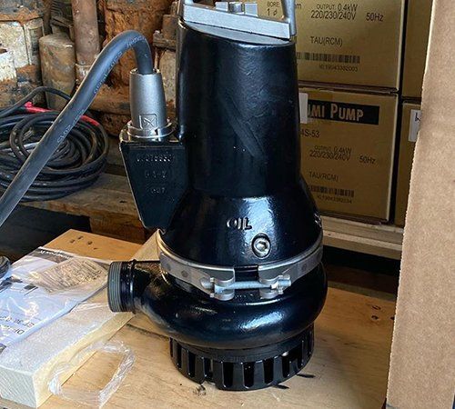 Black submersible pump with handle and power cable, indoors near boxes.