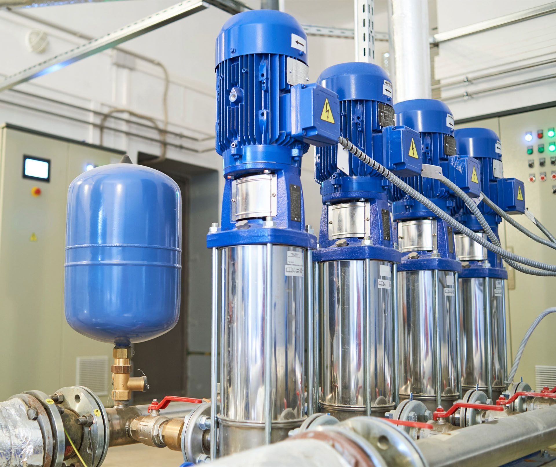 Four blue electric water pumps in a utility room, with a blue pressure tank.