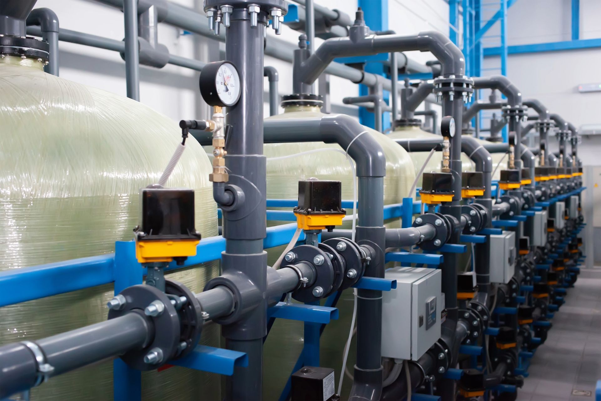 Industrial water filtration system with gray pipes, tanks, and gauges.