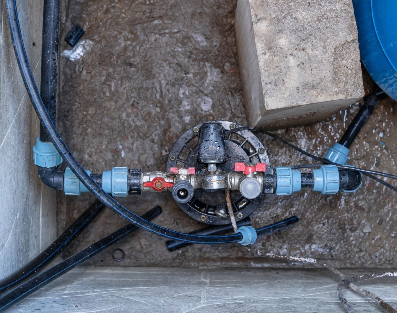 Plumbing with black pipes and blue fittings, red and silver valves on a concrete surface.