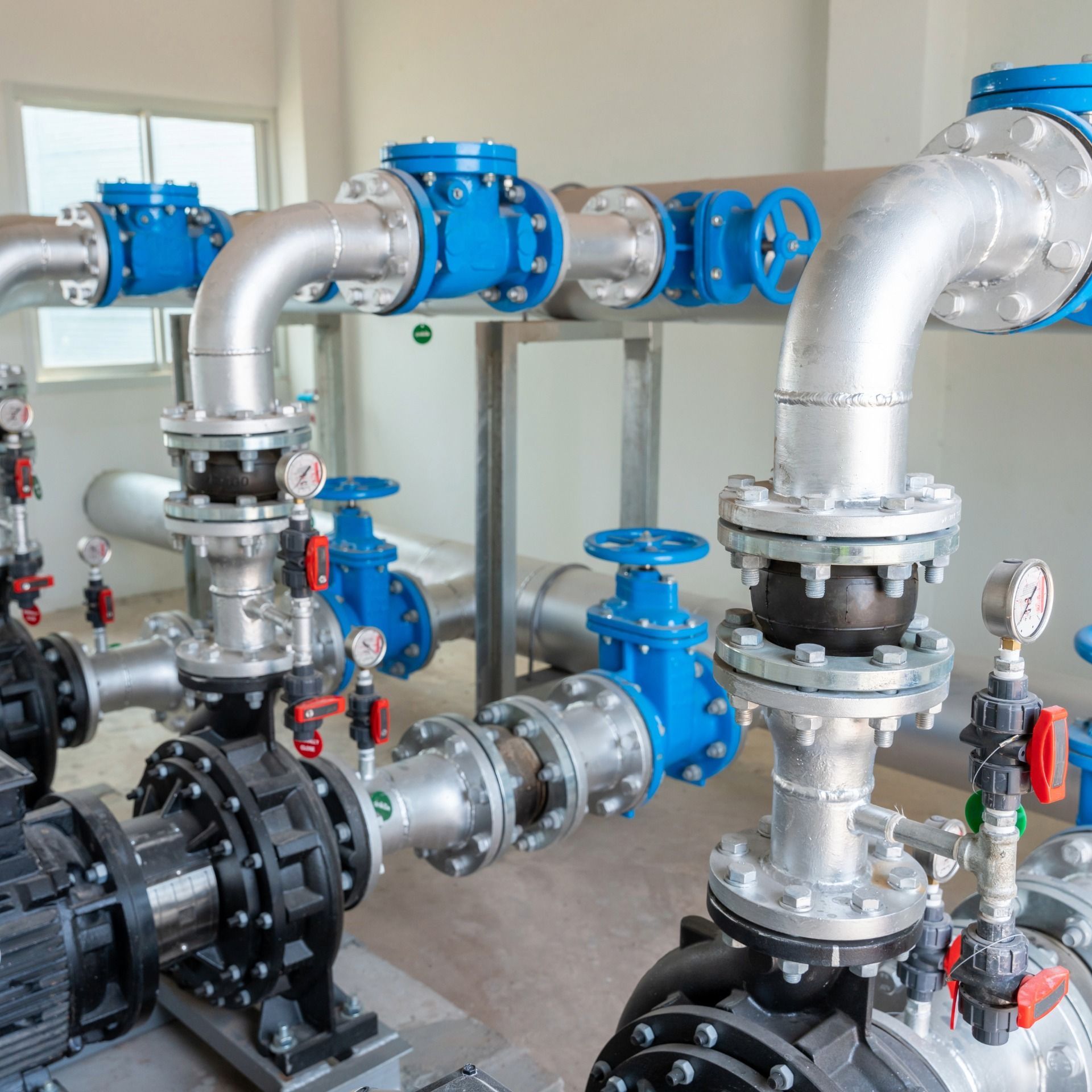 Plumbing system with metallic pipes, blue valves, and black pumps in an industrial setting.