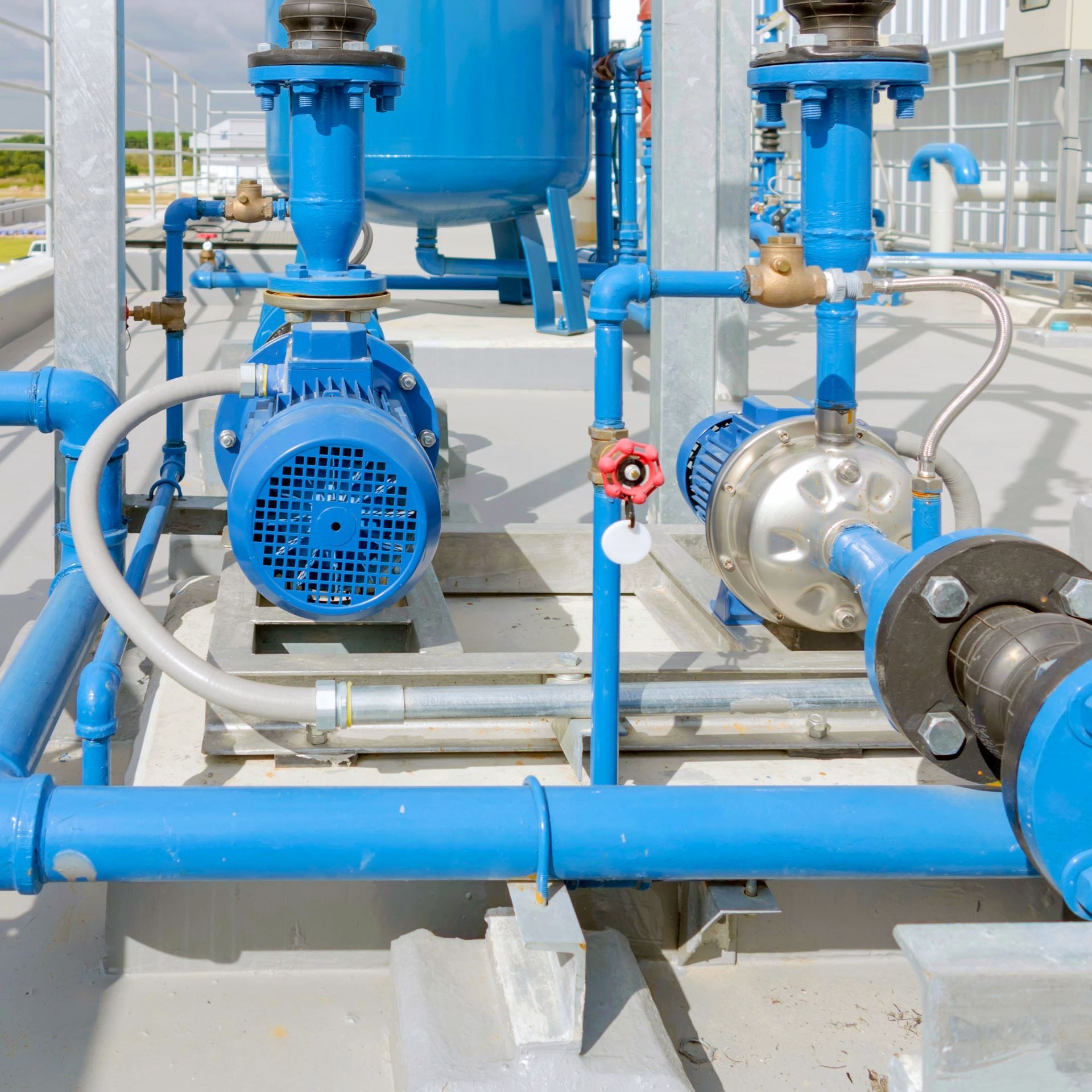 Blue water pumps and piping on a rooftop, with valves and a tank.