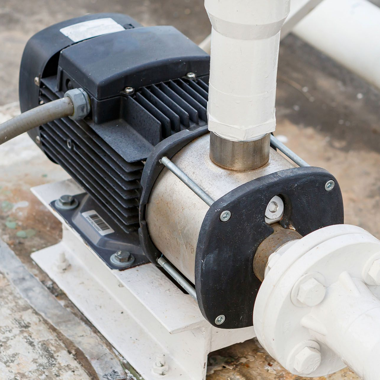 Water pump with electric motor connected to white pipes on a concrete surface.