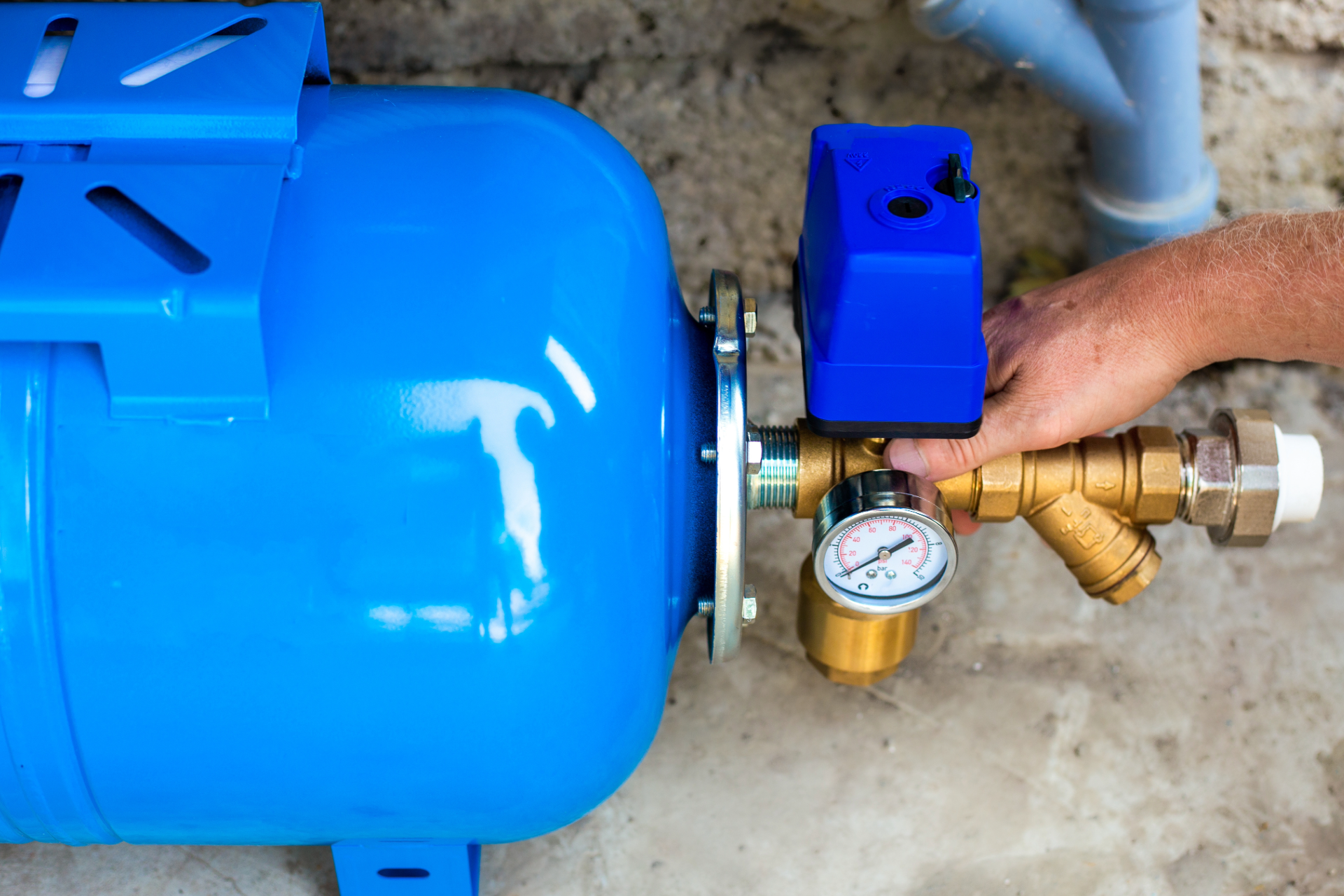 Blue air compressor tank with pressure gauge and brass valve being adjusted by a hand