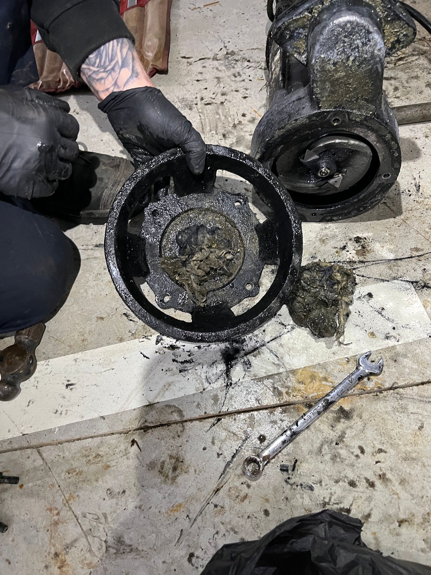 Person holding a disassembled, dirty pump component, showing gears. A wrench lies nearby.