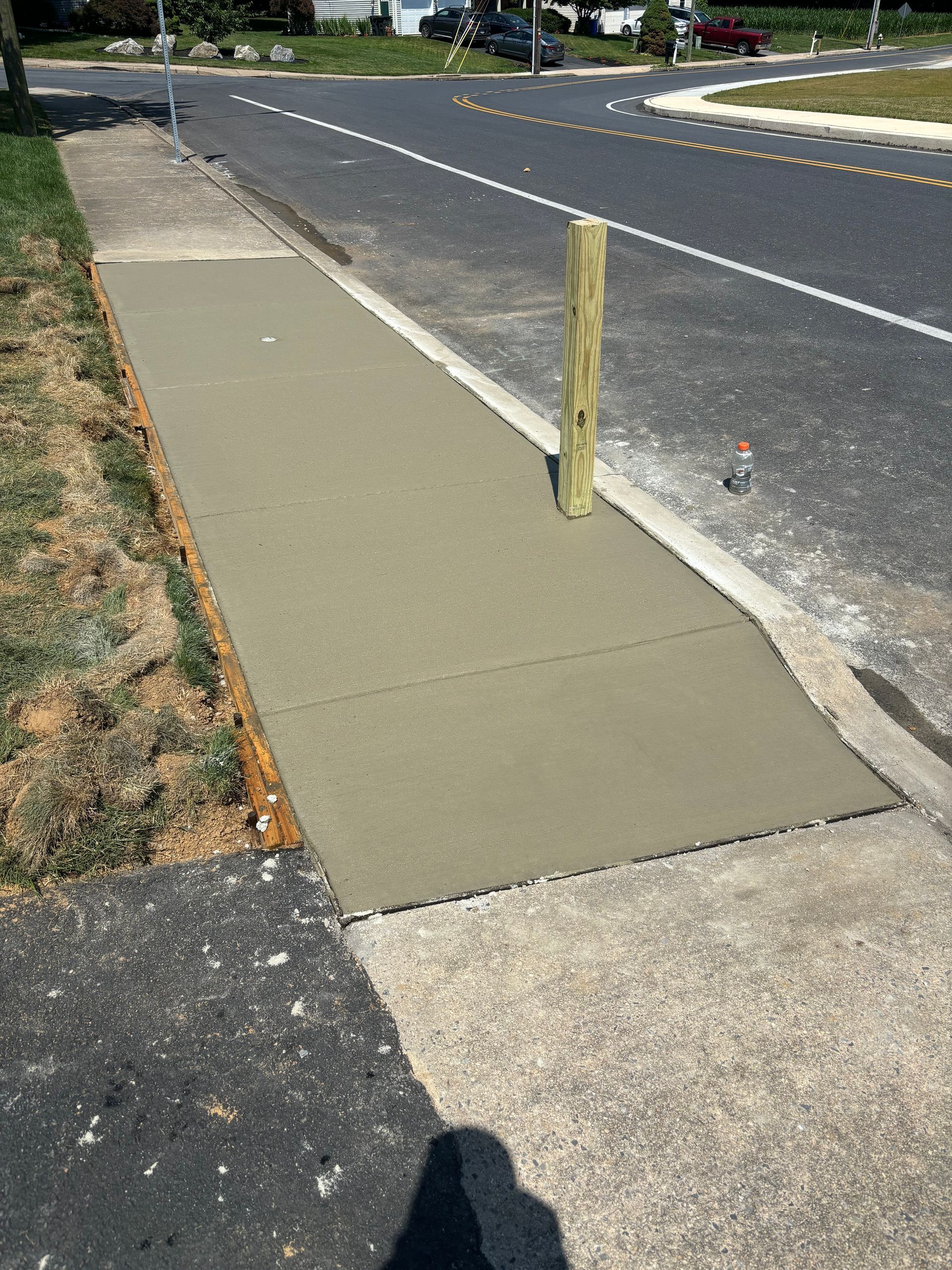 New concrete sidewalk section with a wooden post, next to a street.