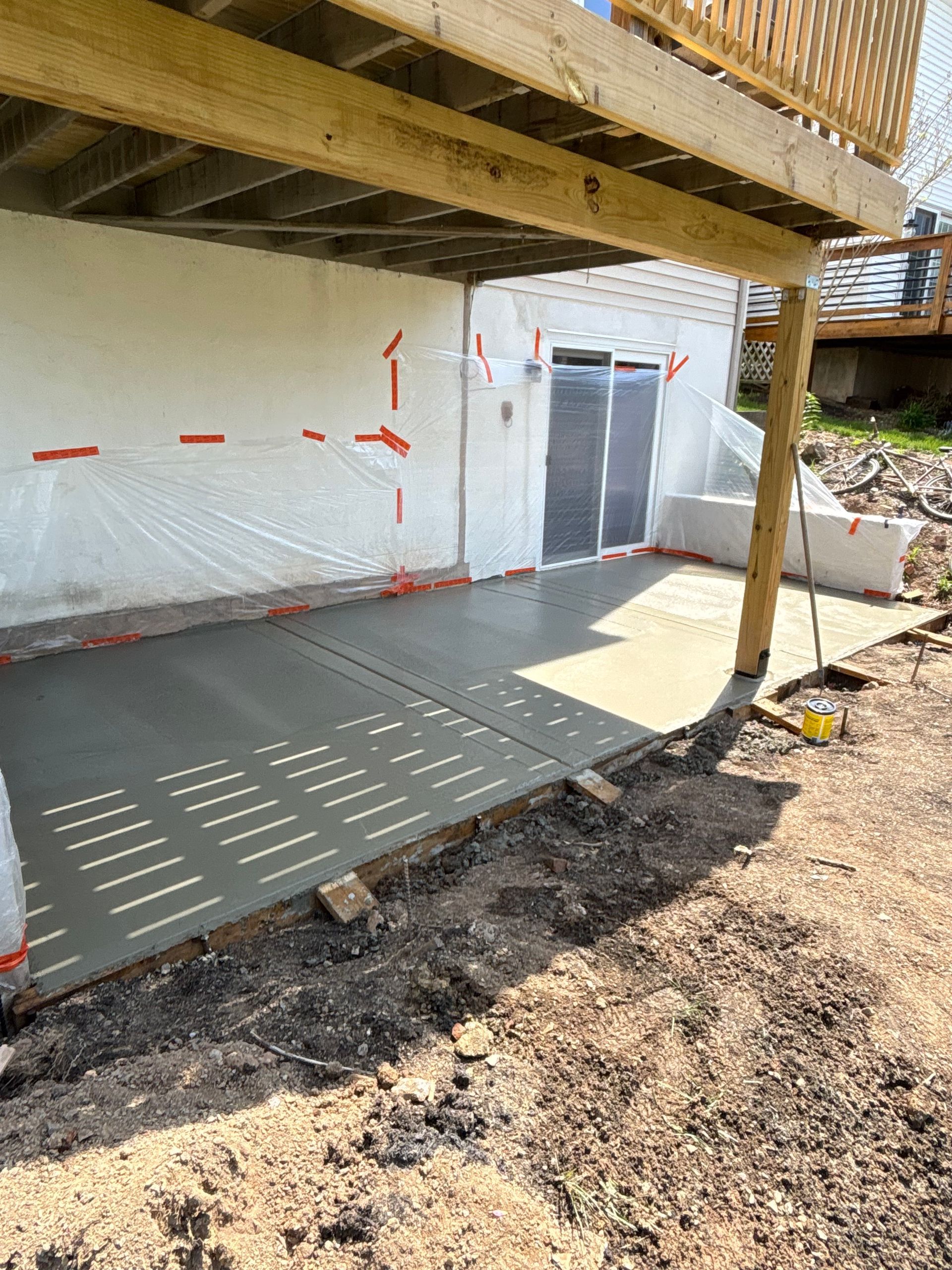 Newly poured concrete patio under a wooden deck with a sliding glass door.