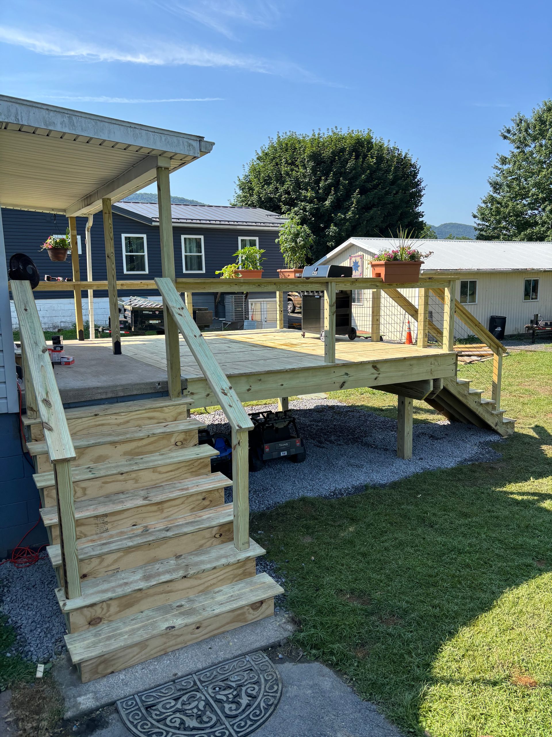 New wooden deck with stairs in a grassy backyard, situated between two houses on a sunny day.