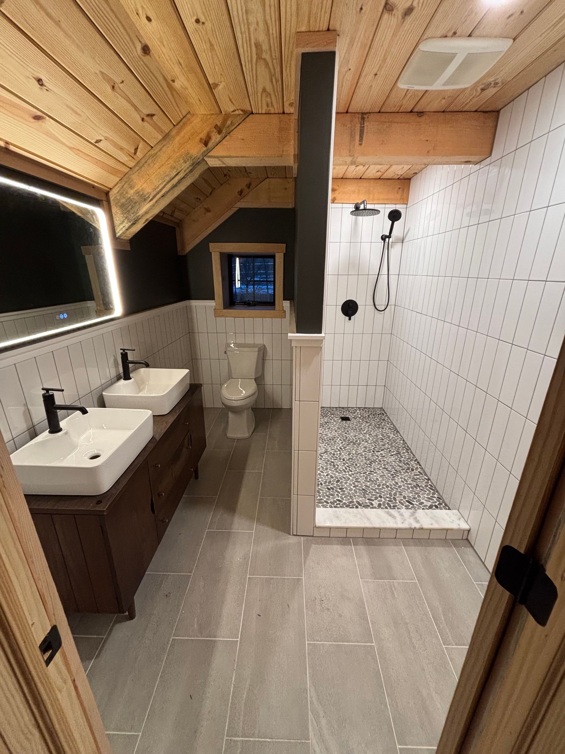 Modern bathroom with wooden ceiling, gray tile floor, double sink, and tiled shower.