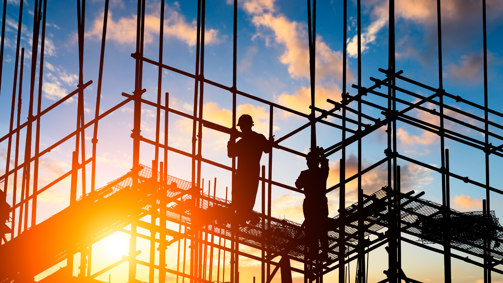 Construction workers on scaffolding at sunset.