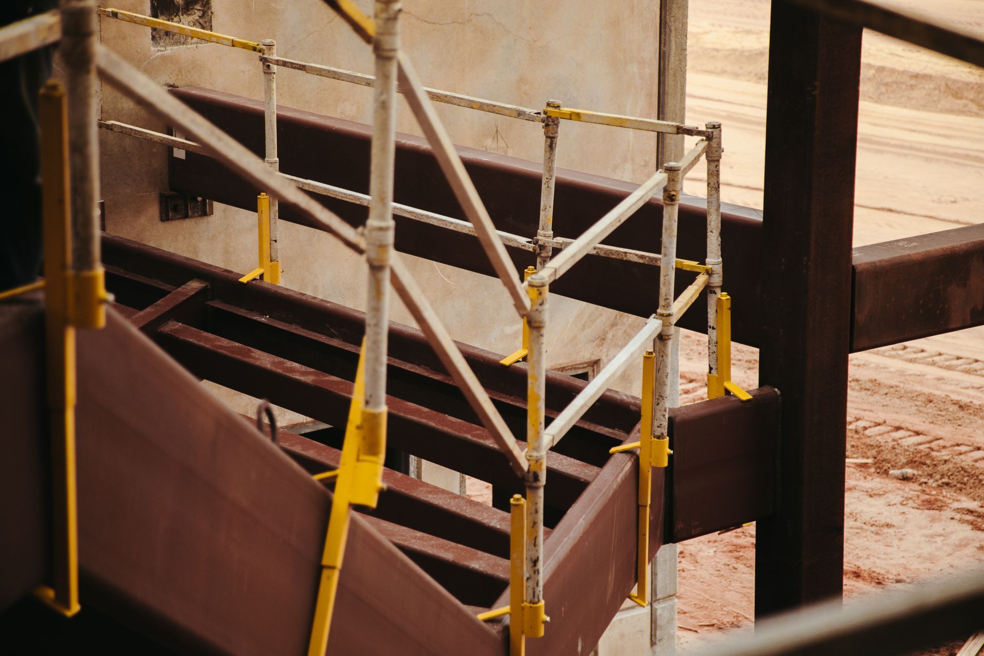 Metal stairs and railings at an industrial site, with yellow safety posts and brown structures.