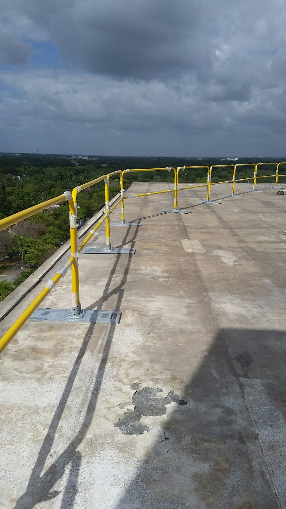 Rooftop concrete platform with yellow railings under a cloudy sky, overlooking a distant landscape