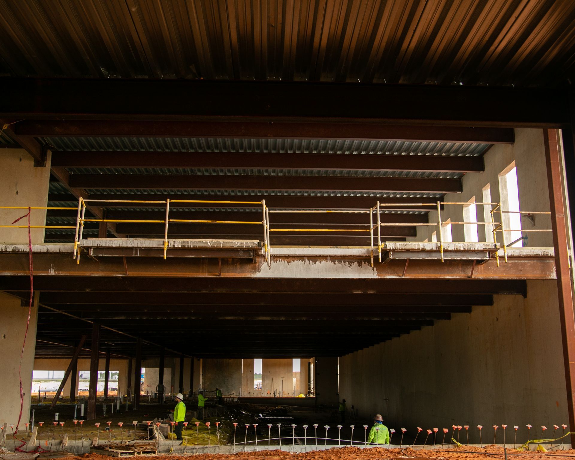 Interior of an unfinished building under construction with workers and scaffolding beneath a large concrete slab