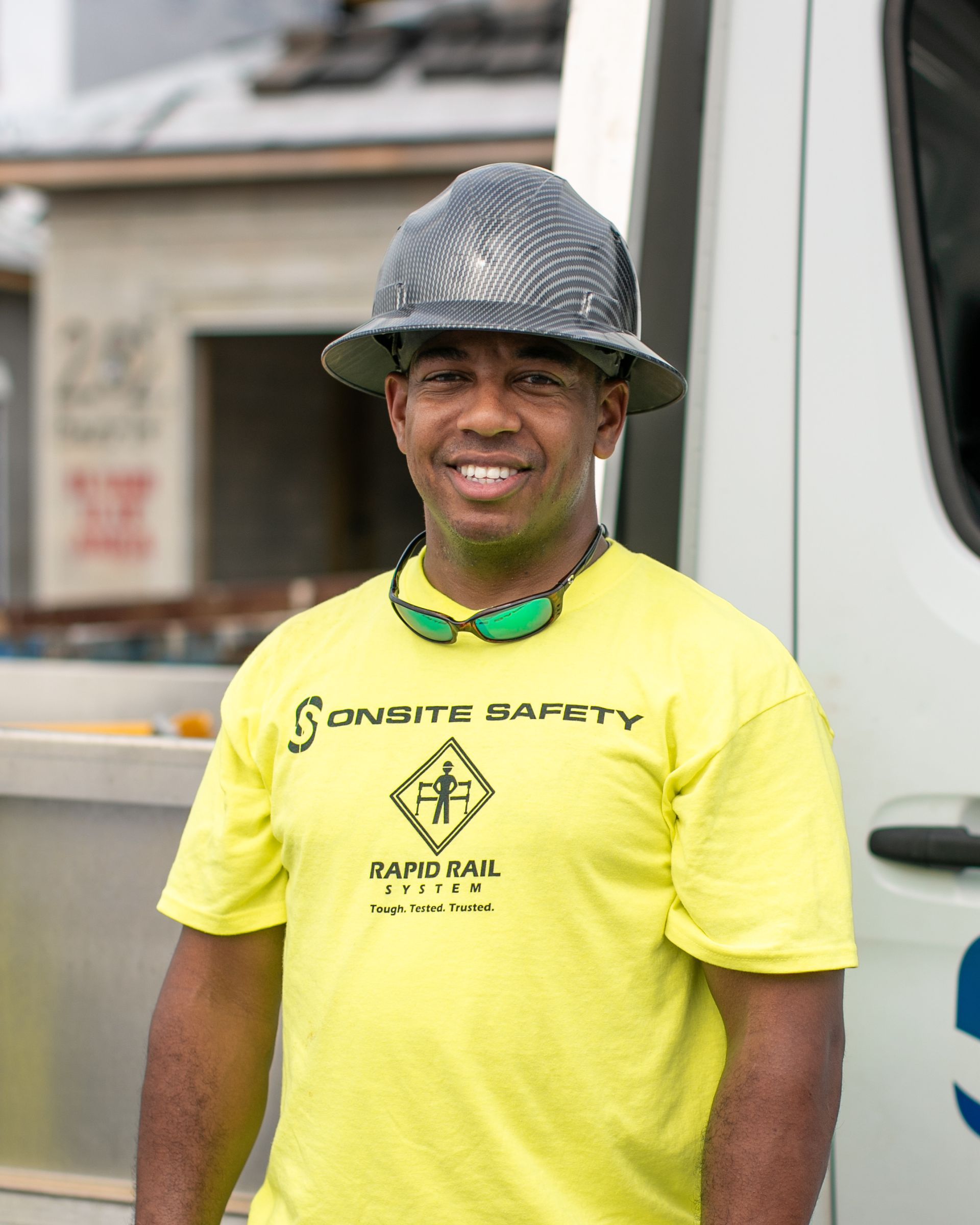 Smiling worker in a neon yellow shirt and hard hat standing beside a white truck