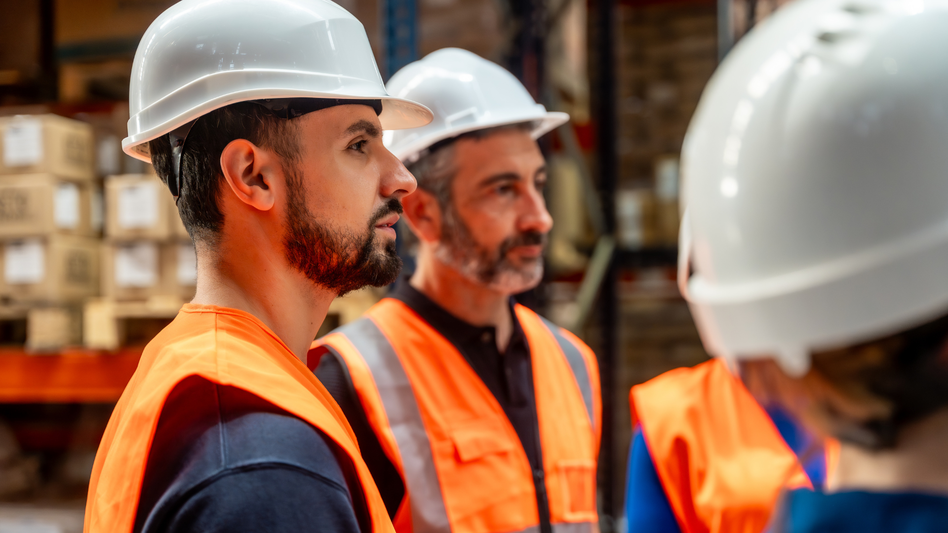 Warehouse workers in hard hats and orange vests.