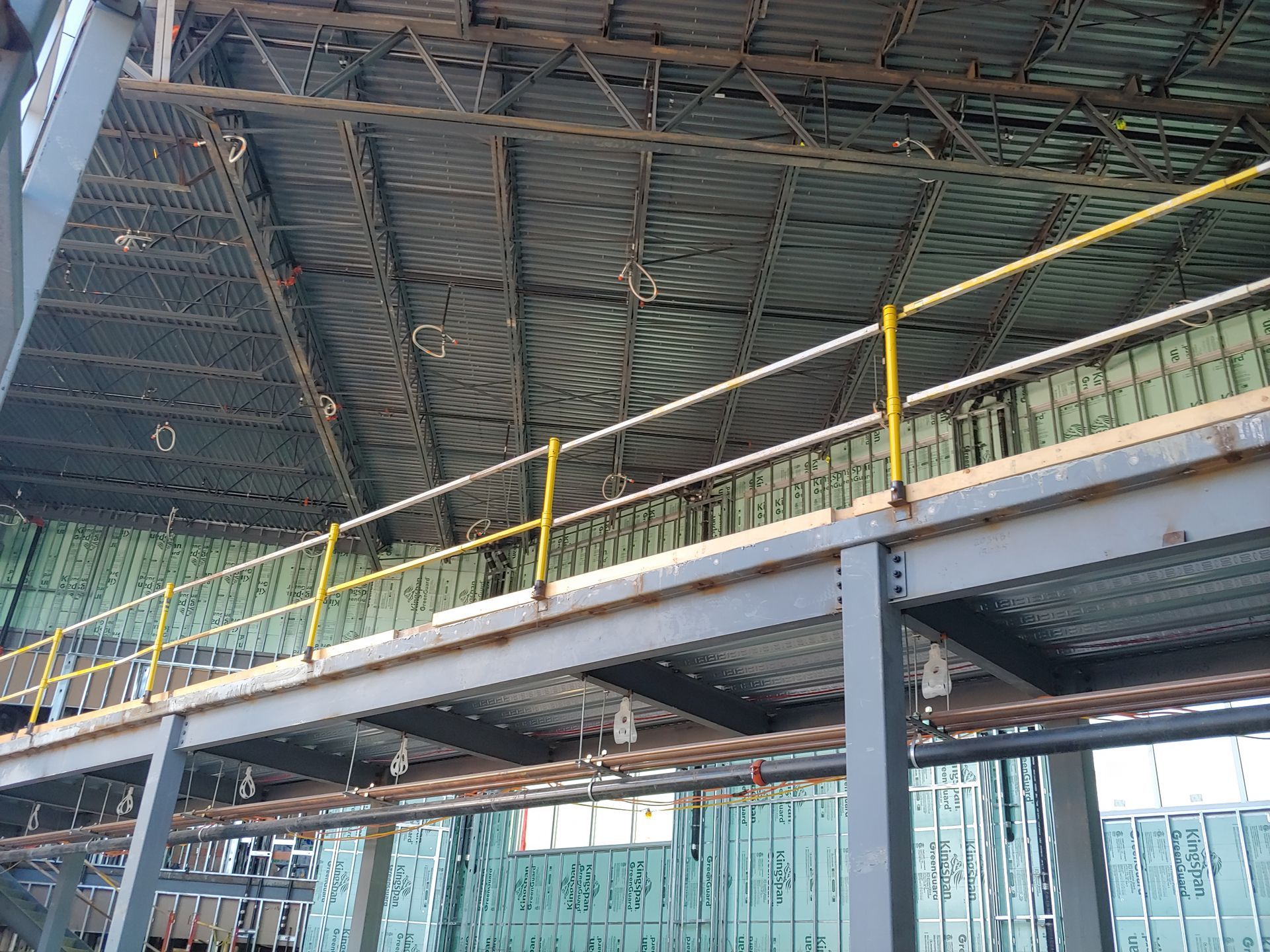 Industrial interior with steel beams, a corrugated roof, and yellow safety railings on an elevated walkway