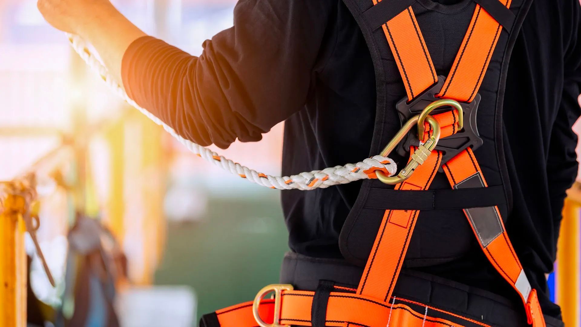 Worker in orange safety harness securing a chain while standing near construction equipment outdoors