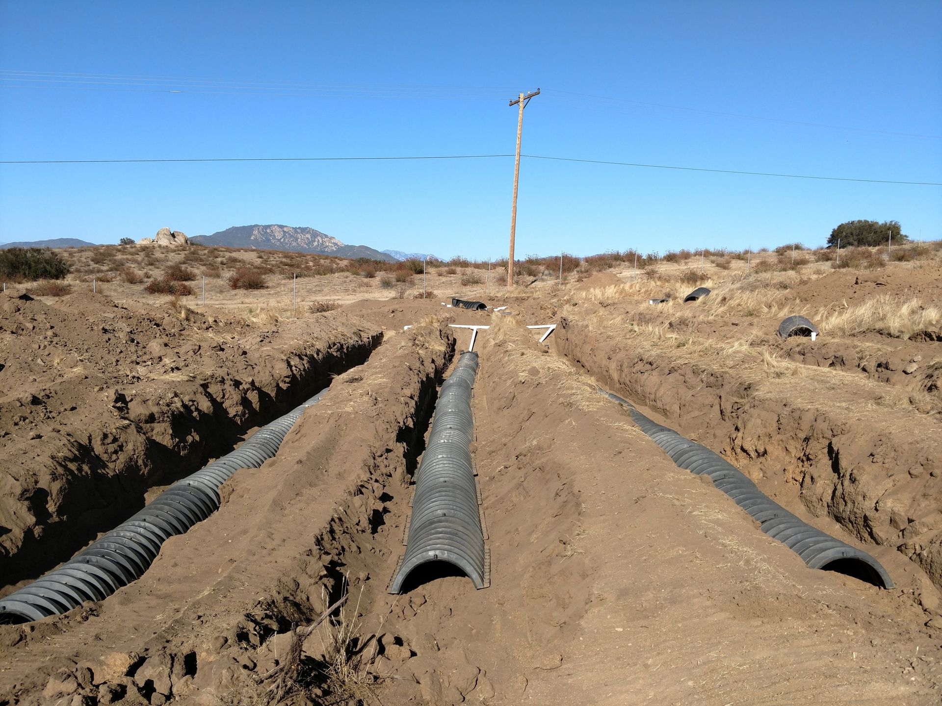 Utility pipes laid in a dirt trench at a construction site under a clear blue sky