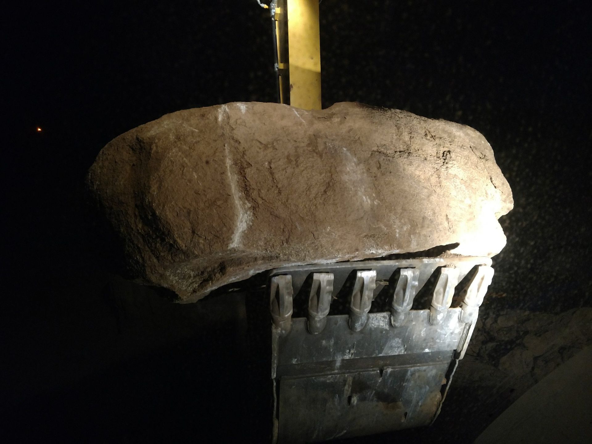 Nighttime close-up of a damaged trash can under a large rock or concrete block