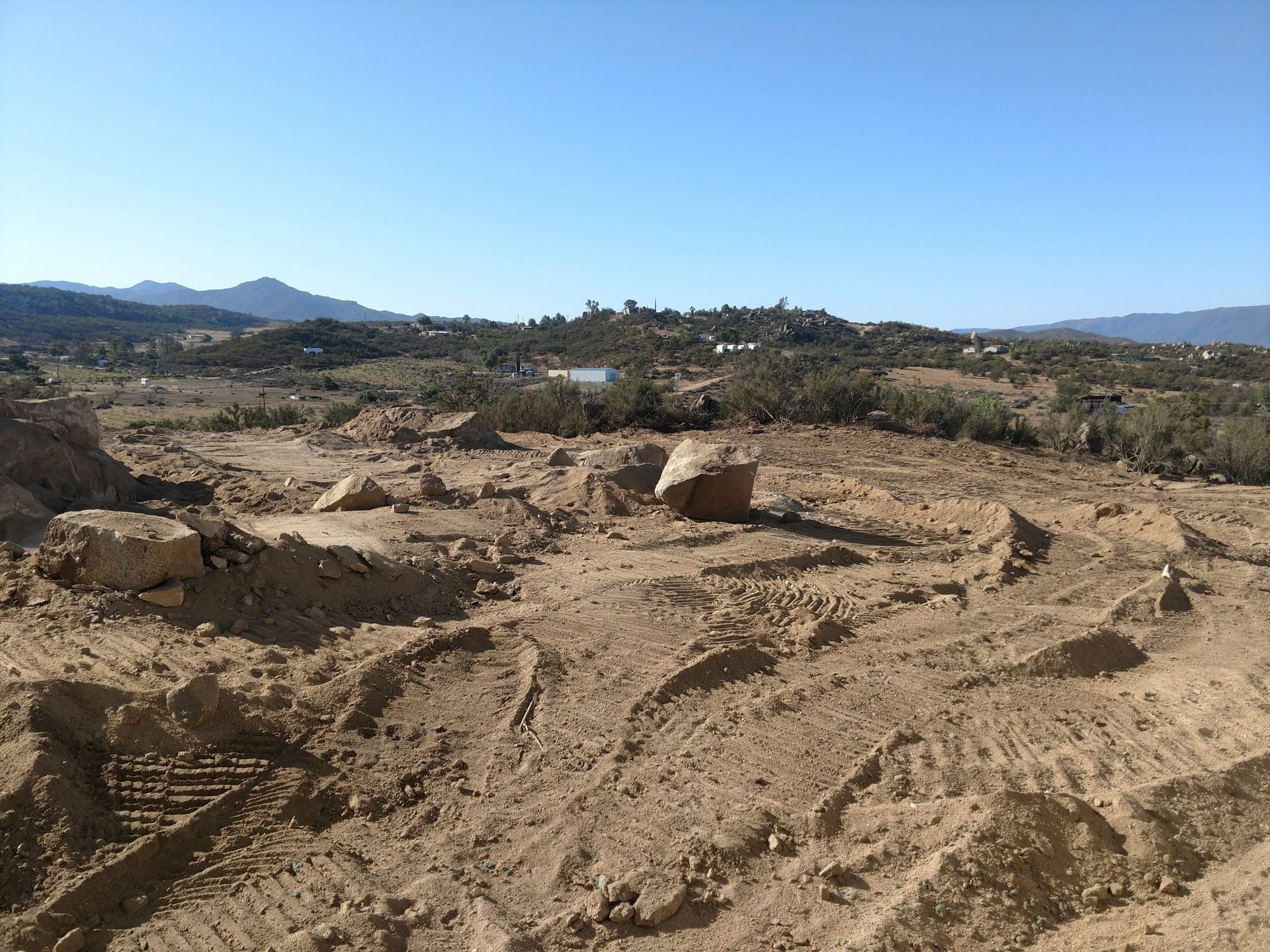 Dry, rocky dirt road through a barren landscape under a clear blue sky, with distant hills.