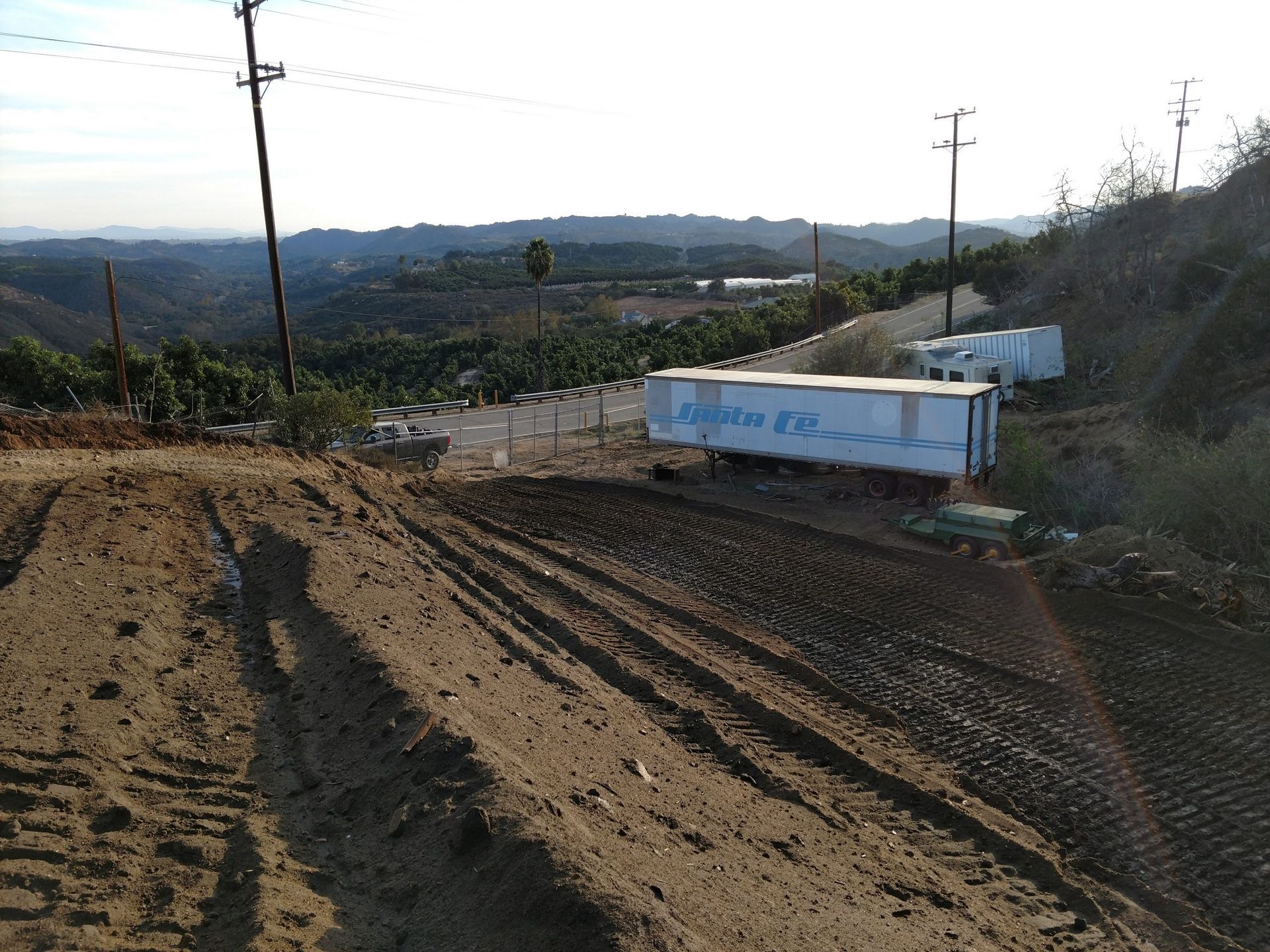 Dirt road with deep tire ruts beside a white truck in a dry rural hillside landscape