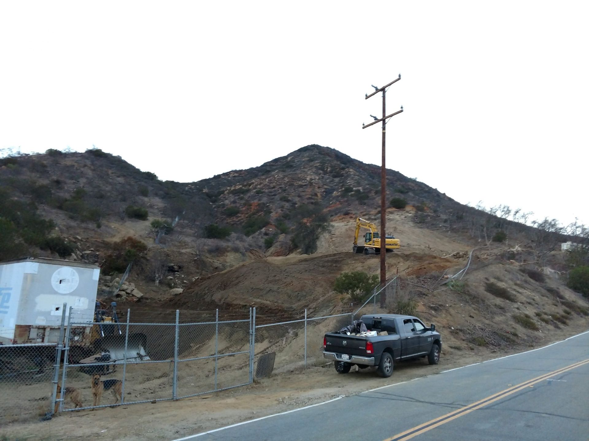 Roadside hillside with power lines, a parked SUV, and a small yellow utility vehicle on the slope