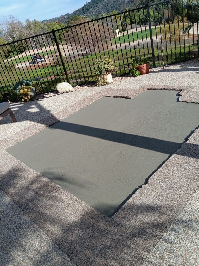 Large dark green mats laid over a gravel patio beside a black fence and potted plants.