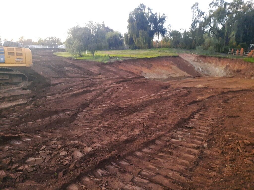 Excavator at a muddy construction site with an excavated dirt pit and trees in the background