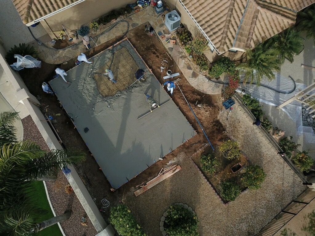 Aerial view of a house roof and fenced yard with workers around a construction or repair site.