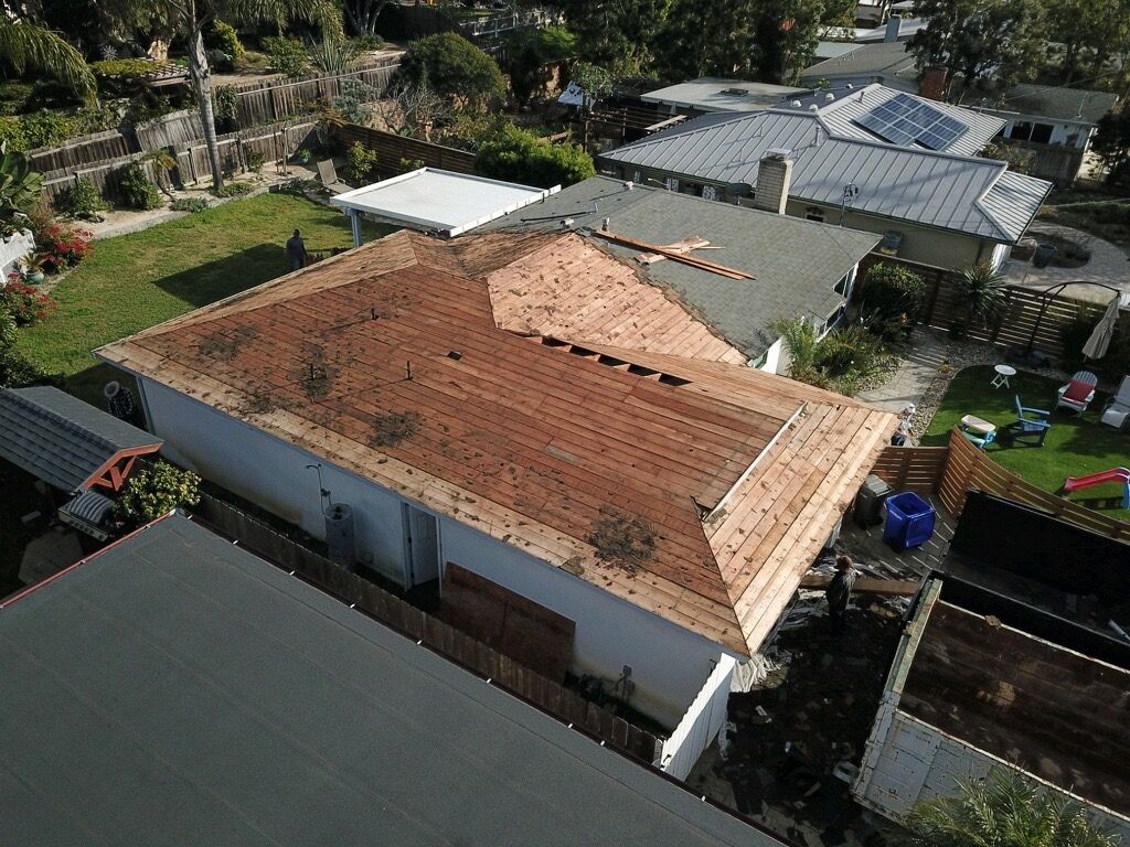 Aerial view of a house with a red tile roof and surrounding neighborhood greenery.