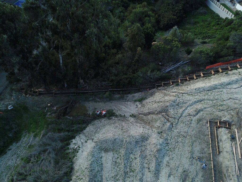 Aerial view of a rocky shoreline with a wooded area and a narrow path or road along the edge