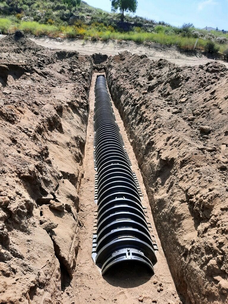Black corrugated pipe laid in a long trench with dirt banks on both sides outdoors