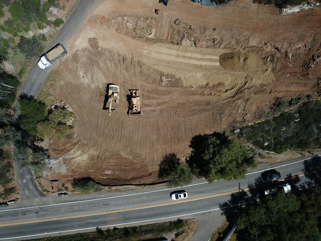 Aerial view of a dirt construction site with heavy equipment beside a road and a truck.