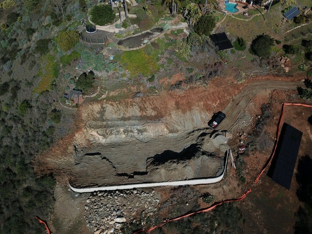 Aerial view of a construction excavation with a concrete foundation, dirt embankments, and a parked truck.