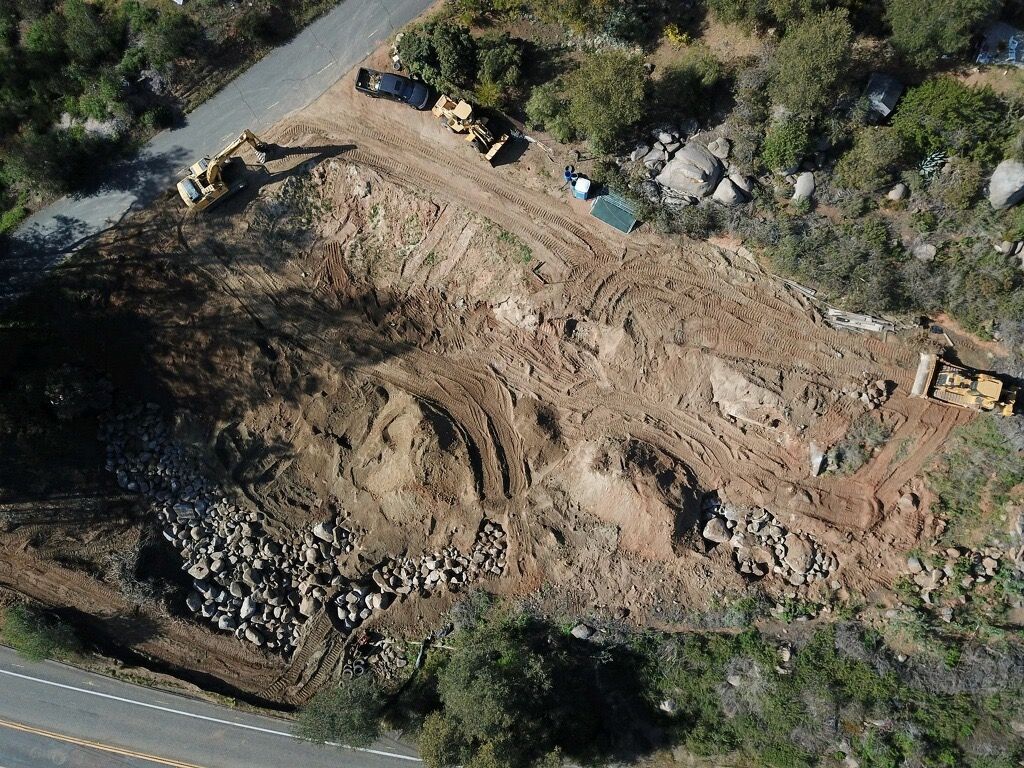 Aerial view of a landslide clearing a hillside road, with heavy machinery and debris beside the road.