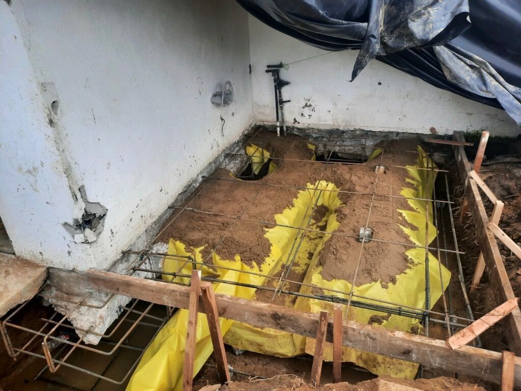 Damaged floor with exposed insulation and debris in a corner of a room under renovation