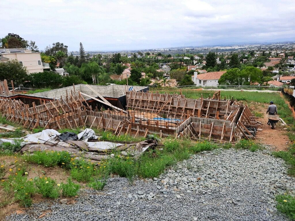 Partially built wooden structure on a hillside with gravel foreground and a city view beyond