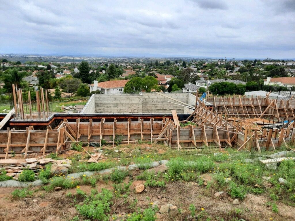 Wide view of a rural hillside with wooden construction, houses, trees, and cloudy sky in the distance