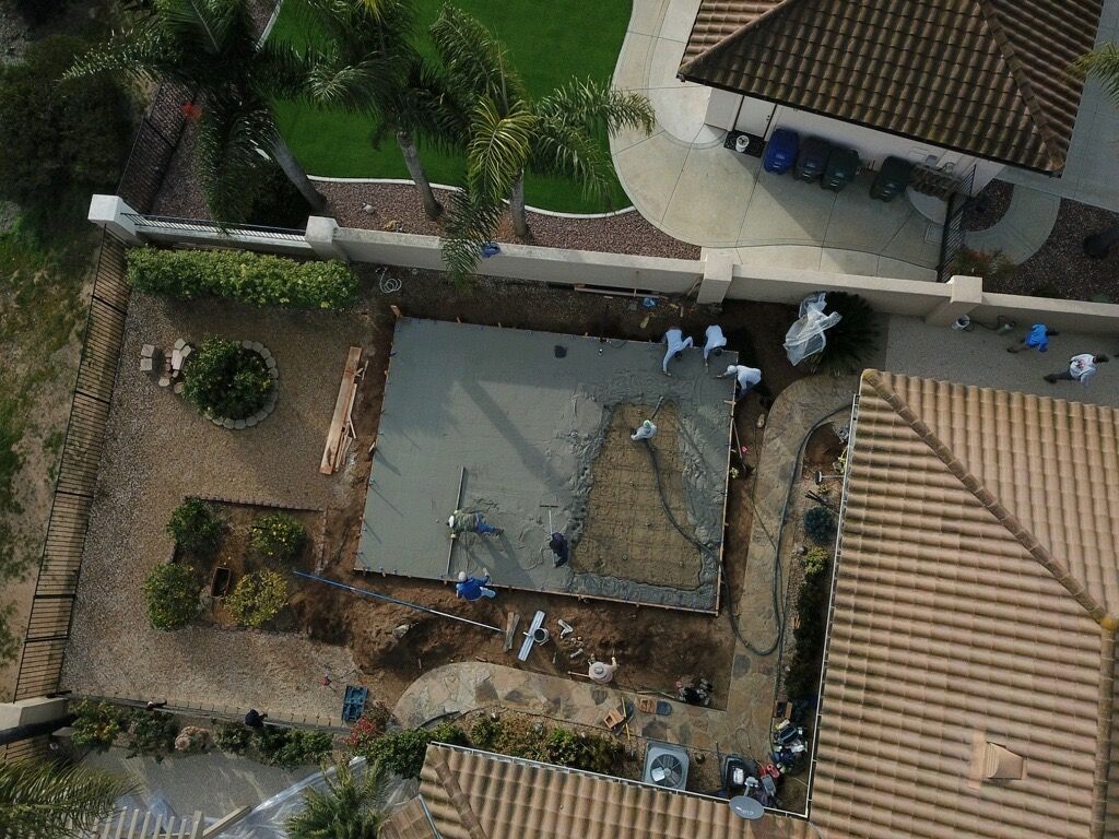 Aerial view of a courtyard with people gathered around a large square pit beside tiled-roof buildings.